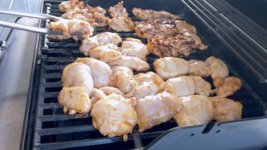 Salamura edilmiş tavuk parçaları pişirme sürecini yakalayan yakın plan bir resim. Bir kişi, klasik bir ızgarada bile pişirmek için ustalıkla onları çeviriyor..