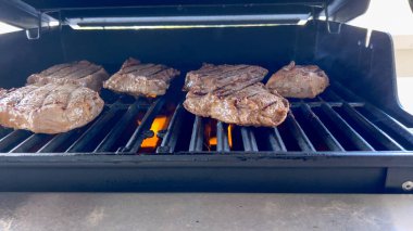 Açık hava ızgarasında ızgara izleri olan birkaç kalın biftek, güneşli bir barbekü gününün özünü yakalıyor..