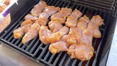 Salamura edilmiş tavuk parçaları pişirme sürecini yakalayan yakın plan bir resim. Bir kişi, klasik bir ızgarada bile pişirmek için ustalıkla onları çeviriyor..