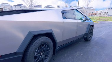 Bir Tesla Siber Traktörü, banliyö sokağında park halindeki kendine özgü, fütüristik tasarımı ve metalik vücuduyla öne çıkıyor. Gelişmiş otomotiv teknolojisinin günlük yaşamla olan karışımını gösteriyor..