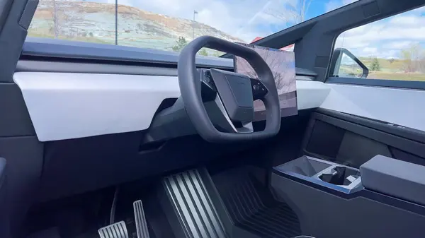 stock image A driver perspective inside the Tesla Cybertruck, highlighting its spacious, minimalist interior with a large touchscreen display and futuristic steering wheel, set against a backdrop of a scenic
