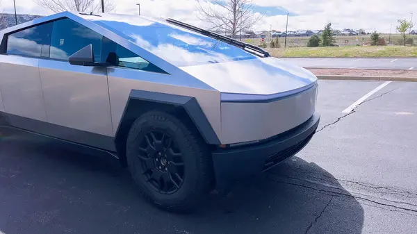 stock image A Tesla Cybertruck stands out with its distinctive, futuristic design and metallic body parked on a suburban street, illustrating the blend of advanced automotive technology with everyday life.