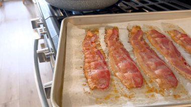 Bu görüntüde, parşömen astarlı fırında pişirilmiş domuz pastırması şeritleri var. Çekici altın-kahverengi rengi ve çıtır çıtır aromasını yakalıyor..