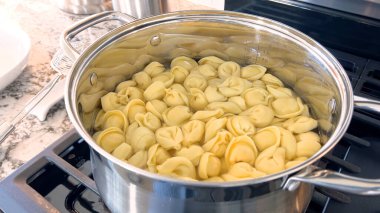 Kaynayan tortellini makarnalarıyla dolu büyük bir tencerede geleneksel İtalyan yemeğinin hazırlıkları sunuluyor. Makarna suyun içinde servis edilmeye hazır, modern bir gaz ocağında..