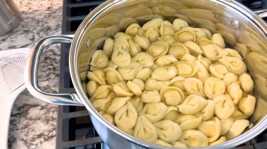 Kaynayan tortellini makarnalarıyla dolu büyük bir tencerede geleneksel İtalyan yemeğinin hazırlıkları sunuluyor. Makarna suyun içinde servis edilmeye hazır, modern bir gaz ocağında..