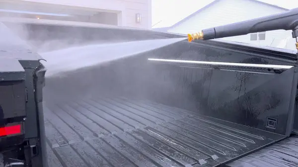 Stock image Denver, Colorado, USA-April 28, 2024- This image captures a Tesla Cybertruck undergoing a thorough cleaning, focusing on the high-pressure washing of its cargo bed, demonstrating the maintenance of