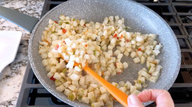A frying pan on a gas stove sizzles with diced potatoes and colorful bits of red and green peppers, showcasing a delicious and simple home-cooked side dish in the making. clipart
