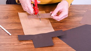 Adım adım. Öğretmen, kahverengi bir çantadan kağıt bir kukla yaparak, çalışma alanı olarak ahşap bir yüzey kullanarak çevrimiçi sınıfa rehberlik ediyor..