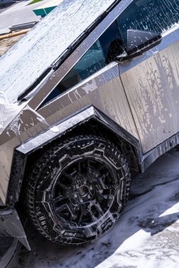 Denver, Colorado, ABD-5 Mayıs 2024 'te yıkanan bir Tesla Cybertruck görüntüsü, aracın açısal tasarımını ve engebeli lastiklerini gösteriyor. Su ve sabun köpükleri metalik yüzeyi kaplar.
