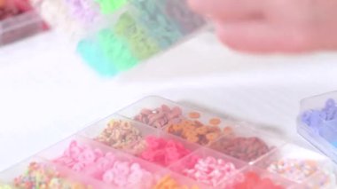 Parlak renkli balçık boncuklarından oluşan geniş bir koleksiyonu bölümlere ayıran eller, karmaşık malzemelerin güzelliğini ve çeşitliliğini vurguluyor.