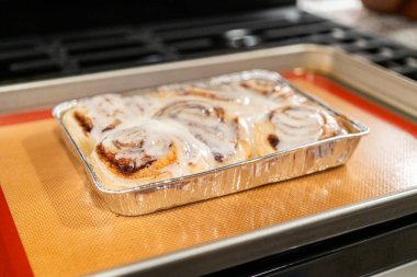 Fırından yeni çıkmış, tarçınlı çörek silikon bir hasırın üzerinde serinliyor, kremaları mutfak ışıklarının altında parlıyor..