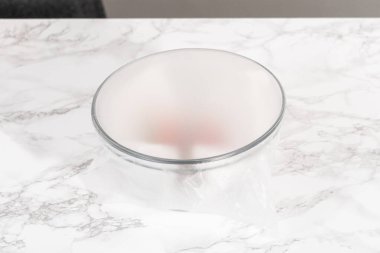 Çilekler, yeni yıkanmış ve kurutulmuş, cam bir kasede güzelce depolanmış kağıt havluyla kaplanmış ve tazeliği korumak için plastikle kaplanmış..