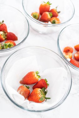 Parlak kırmızı çilekler, küf izleriyle karışmış, beyaz peçetedeki kağıt havluyla kaplı cam bir kasede dinleniyor, depolama tekniklerini gösteriyor..