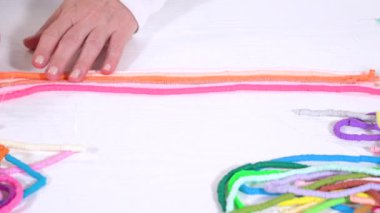 Eller birbirine zıt beyaz bir yüzeye karşı düzgün düzenlenmiş renkli, sarmalanmış kil boncuk iplikçiklerine dokunur..