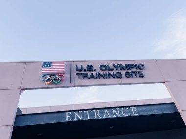 Colorado Springs, Colorado, ABD-13 Mayıs 2024 ABD Olimpiyat Eğitim Alanının giriş işaretinin detaylı bir görüntüsü, açık bir gökyüzü altında Amerikan bayrağı ve Olimpiyat halkaları yer alıyor..