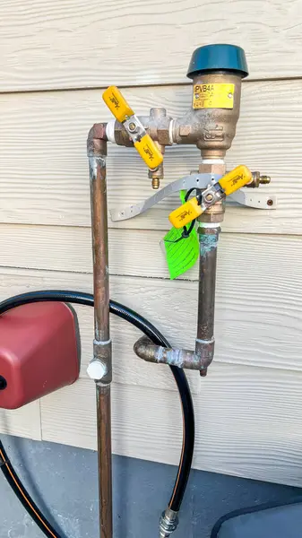 stock image Denver, Colorado, USA-October 17, 2023-Close-up image of an outdoor residential plumbing system attached to a house wall, featuring a backflow preventer and valve setup. This setup is essential for