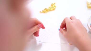 Genç kız derinden bilezik yapma sanatına odaklanmış. Canlı kil boncukları eşsiz kalıplara döküyor. Çalışma alanı çeşitli boncuklarla düzenlenmiş. Bu da nişanını gösteriyor.