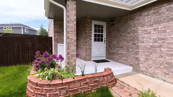 stock image The front porch of a charming brick house featuring a white door and a well-maintained garden bed with blooming purple flowers. The neatly trimmed lawn and inviting entryway enhance the home curb