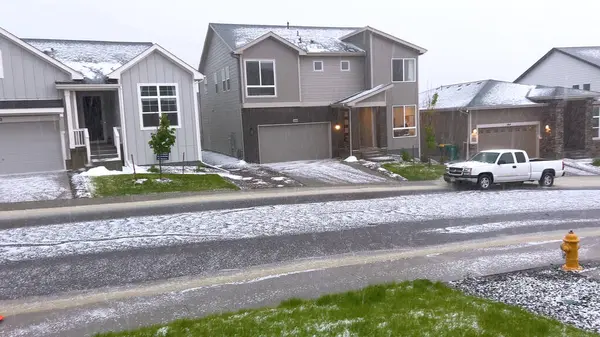 stock image Castle Rock, Colorado, USA-June 12, 2024-Slow motion-A suburban neighborhood with modern houses covered in a layer of hail after a storm. The scene shows a driveway with a car parked, and the street