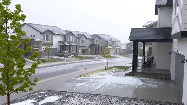 stock image Castle Rock, Colorado, USA-June 12, 2024-Slow motion-A suburban neighborhood with modern houses covered in a layer of hail after a storm. The scene shows a driveway with a car parked, and the street