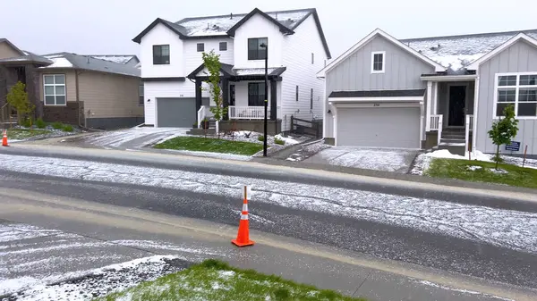 stock image Castle Rock, Colorado, USA-June 12, 2024-Slow motion-A suburban neighborhood with modern houses covered in a layer of hail after a storm. The scene shows a driveway with a car parked, and the street