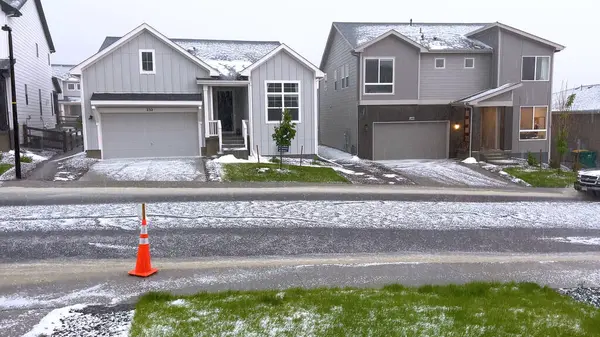 stock image Castle Rock, Colorado, USA-June 12, 2024-Slow motion-A suburban neighborhood with modern houses covered in a layer of hail after a storm. The scene shows a driveway with a car parked, and the street