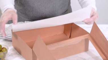 Elleri titizlikle bir kaseye taze kırmızı üzüm ekliyor, çeşitli peynirler, zeytinler ve pişirilmiş etlerle dolu güzel bir şarküteri kutusunu tamamlıyor.