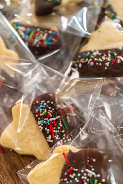 Dikkatlice paketlenmiş Noel kurabiyeleri, çikolataya batırılmış ve şeffaf selofan ambalajla sunulmuş, bayram hediyesi olarak mükemmel..