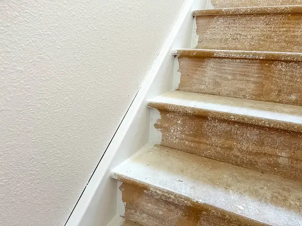 stock image A detailed close-up image of a staircase undergoing renovation, showcasing unfinished steps and wall repairs. The steps are covered in construction dust, and patches of the wall are visibly marked for