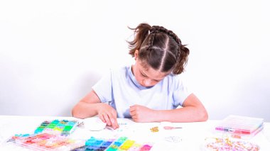 Genç bir kızın narin parmakları parlak, renkli boncuklardan oluşan bir hazinede geziniyor. Her bölümde seçilecek yeni bir renk var. Neşeli bir vazifeye daldı.