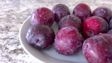 Bir dekoratif tabakta sergilenen olgun, parlak erik koleksiyonu, canlı kırmızı ve mor renkler sergileniyor, mutfak tezgahının üzerinde..