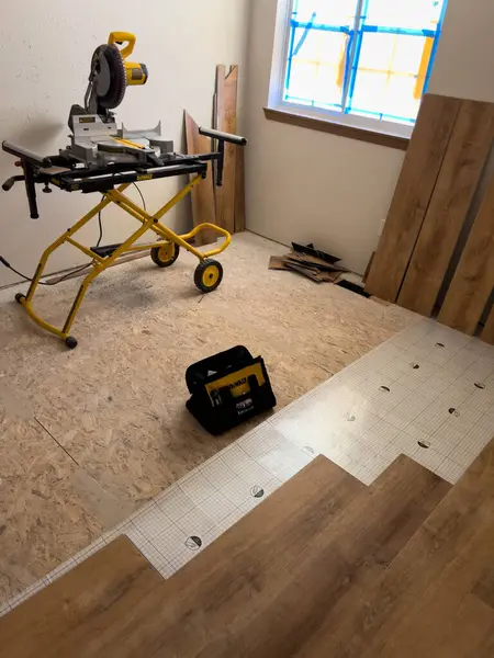 stock image The image shows a miter saw set up on a yellow stand, ready for use in a room undergoing renovation. The partially installed wood floor and construction materials indicate ongoing flooring work. The