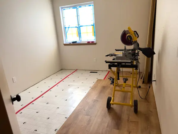 stock image Broomfield, Colorado, USA-July 14, 2024- The image shows a miter saw set up on a yellow stand, ready for use in a room undergoing renovation. The partially installed wood floor and construction