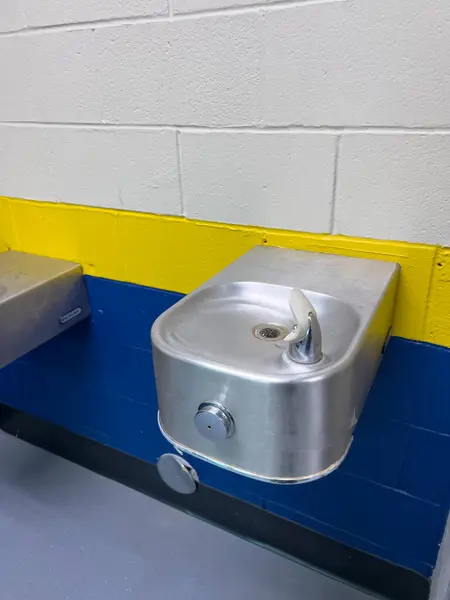 Stock image Denver, Colorado, USA-July 12, 2024-Two metal drinking fountains attached to a wall painted with blue and yellow stripes in a public facility, providing a clean and functional hydration station.