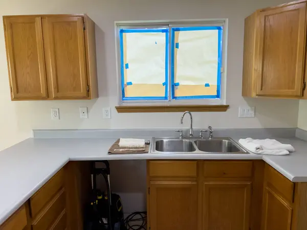 stock image Broomfield, Colorado, USA-July 6, 2024-A kitchen undergoing renovation, featuring wooden cabinets and an unfinished plywood floor. The countertops are installed, and the window is taped for painting