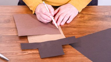 Adım adım. Öğretmen, kahverengi bir çantadan kağıt bir kukla yaparak, çalışma alanı olarak ahşap bir yüzey kullanarak çevrimiçi sınıfa rehberlik ediyor..