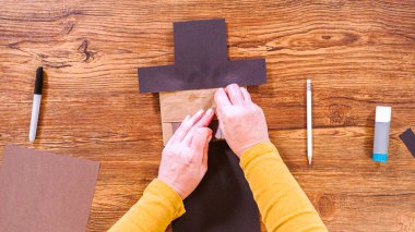 Adım adım. Düz yatıyordu. Öğretmen, kahverengi bir çantadan kağıt bir kukla yaparak, çalışma alanı olarak ahşap bir yüzey kullanarak çevrimiçi sınıfa rehberlik ediyor..