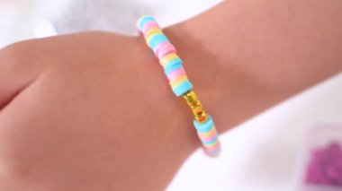 Genç kız derinden bilezik yapma sanatına odaklanmış. Canlı kil boncukları eşsiz kalıplara döküyor. Çalışma alanı çeşitli boncuklarla düzenlenmiş. Bu da nişanını gösteriyor.