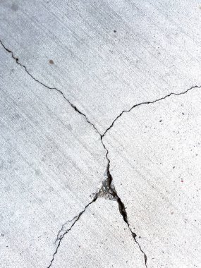 Çatlak bir beton yüzeyin yakın çekimi, belirgin çizgiler ve çatlaklar gösteriyor. Betonun dokusu aşınmayı ve zamanla oluşan hasarı açıkça gösteriyor. Bu resim ham olanı yakalar.