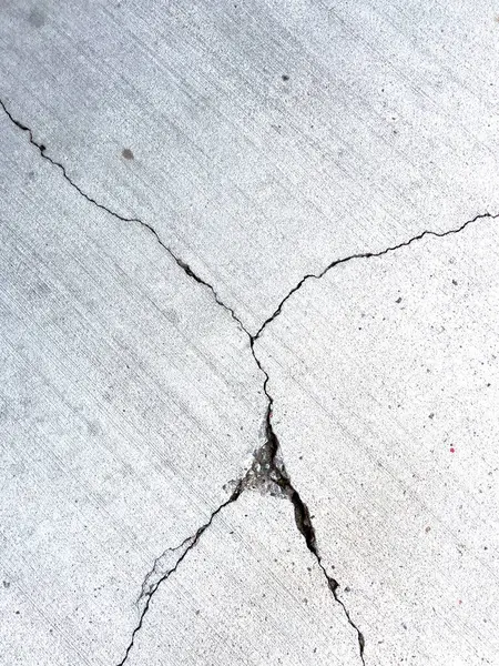 Çatlak bir beton yüzeyin yakın çekimi, belirgin çizgiler ve çatlaklar gösteriyor. Betonun dokusu aşınmayı ve zamanla oluşan hasarı açıkça gösteriyor. Bu resim ham olanı yakalar.