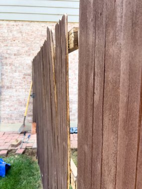 Arka bahçedeki ahşap çitler paneller arasında küçük bir boşluk gösteriyor. Zamanla yıpranmış kahverengi çit, boşluktan görülebilen güneşli çimenler tarafından vurgulanıyor. Bu görüntü kırsal cazibeyi yakalar.