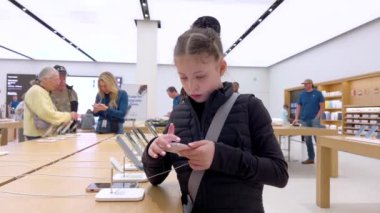 Denver, Colorado, ABD-9 Nisan 2024-10 yaşındaki bir kız dikkatle Apple Store 'daki bir stantta sergilenen yeni bir iPhone' u keşfediyor.