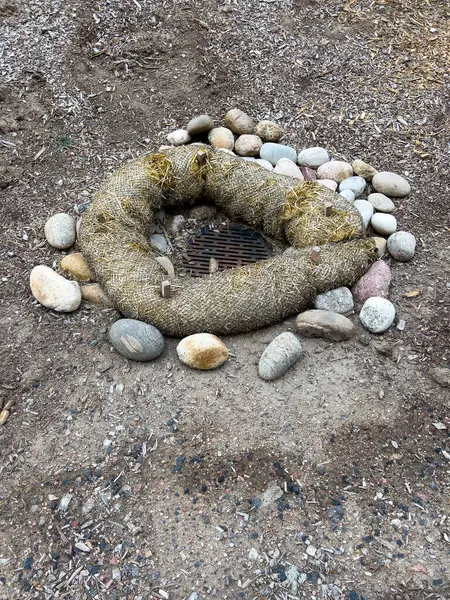 stock image This image depicts an outdoor drainage system protected by erosion control measures. The drain is surrounded by a circular barrier made of natural fiber rolls and large river rocks. The setup ensures