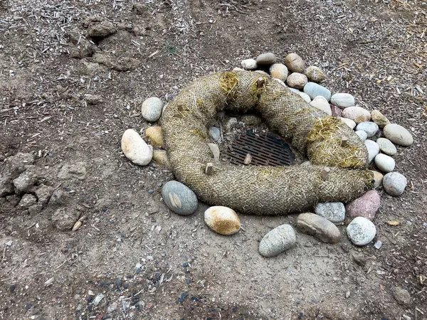 stock image This image depicts an outdoor drainage system protected by erosion control measures. The drain is surrounded by a circular barrier made of natural fiber rolls and large river rocks. The setup ensures