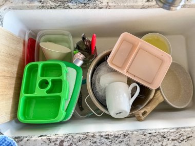 Castle Rock, Colorado, ABD-29 Temmuz 2024. Bu görüntü, sabunlu su dolu bir lavabo ve yıkanmayı bekleyen çeşitli bulaşık ve çatal bıçaklarla tipik bir mutfak sahnesini çekiyor. Ögeler arasında bir yeşil