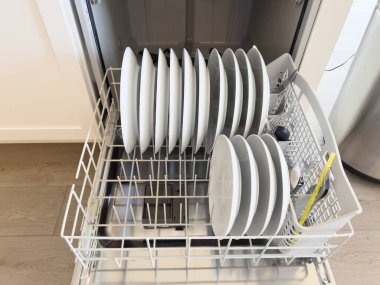 Bu resim temiz beyaz tabaklarla dolu bir bulaşık makinesini sergiliyor. Tabaklar üst rafa yerleştirilirken, tabaklar da üst rafa konur. Organize düzen gösteriyor ki...