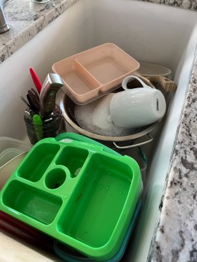 Castle Rock, Colorado, ABD-29 Temmuz 2024. Bu görüntü, sabunlu su dolu bir lavabo ve yıkanmayı bekleyen çeşitli bulaşık ve çatal bıçaklarla tipik bir mutfak sahnesini çekiyor. Ögeler arasında bir yeşil