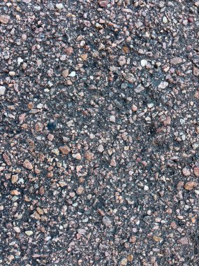 Soluk beyaz çizgi işaretli asfalt bir yol yüzeyine yakın çekim. Asfaltın kaba dokusu, içine yerleştirilmiş küçük taşlar ve çakıl taşlarının karışımı ile vurgulanır ve aşınma izleri gösterir.