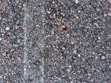 Soluk beyaz çizgi işaretli asfalt bir yol yüzeyine yakın çekim. Asfaltın kaba dokusu, içine yerleştirilmiş küçük taşlar ve çakıl taşlarının karışımı ile vurgulanır ve aşınma izleri gösterir.