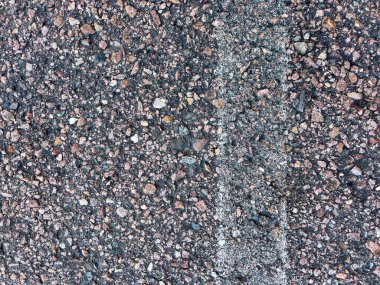 Soluk beyaz çizgi işaretli asfalt bir yol yüzeyine yakın çekim. Asfaltın kaba dokusu, içine yerleştirilmiş küçük taşlar ve çakıl taşlarının karışımı ile vurgulanır ve aşınma izleri gösterir.